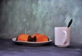 A plate with three poppy seed buns and a cup of hot drink with a spoon on a gray abstract background
