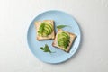 Plate with toasts with avocado, arugula and sesame on background, top view