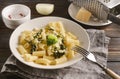 Plate with tortilloni with sauce and spinach and cheese, broccoli, fork, napkin, cheese grater on a light background, spinach