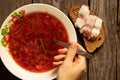 a plate with traditional Ukrainian borscht and a piece of bread with bacon on a side wooden table