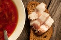 a plate with traditional Ukrainian borscht and a piece of bread with bacon on a side wooden table