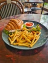 A plate of tuna croissant sandwich with frenc fries