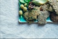 Plate with vegan snacks like linnen crackers, olives, avocado, cucumbers, walnuts and a wooden fork placed on a rough fabric