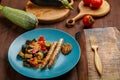 A plate of vegetables with grilled sausages on the table next to zucchini on wooden boards and a wooden fork