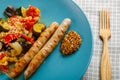 A plate of vegetables tomatoes zucchini eggplant with grilled sausages next to a wooden fork close-up. Royalty Free Stock Photo