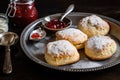 plate of warm scones, topped with scoop of strawberry jam and a dusting of powdered sugar