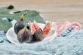 A plate of whole and sliced black figs, a leaf and blue and pink tablecloths on a wooden table, close up