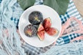 A plate of whole and sliced black figs, a leaf and blue and pink tablecloths on a wooden table