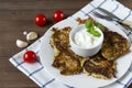 Plate with zucchini pancakes with sour cream and herbs on a wooden background