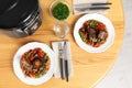 Plates with meat and garnish prepared in multi cooker on wooden table Royalty Free Stock Photo