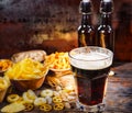 Plates with snacks near two bottles and a glass of freshly poured dark beer, wheat, scattered nuts and pretzels on dark wooden de Royalty Free Stock Photo