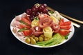 A platter with assortment of sliced ham and cheese with vegetables and grape on black background Royalty Free Stock Photo