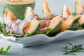 A platter of cantaloupe wedges wrapped in prosciutto, ready for eating.