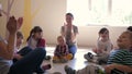 Play with educators, group of cute young kids applaud with adults sit in a circle in kindergarten