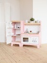 Play furniture for children. Wooden pink and white kitchen with fridge, stove, oven and sink in light room