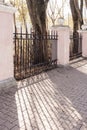 Play of light and shadows on stone sidewalk through fence lattice on autumn day.