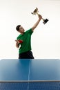 Player in victory pose holds cup and racquet at table tennis match against white studio background. Power and strength.