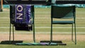 Players` chairs with towel folded over the back, and a green and purple umbrella on the ground. Towel has the name Djokovic on it