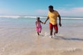 Playful african american young father and daughter holding hands and running in sea against sky Royalty Free Stock Photo