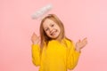 Playful angelic little girl raising arms and looking at camera with toothy smile, gesturing oops, i don`t know Royalty Free Stock Photo