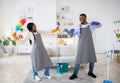 Playful black couple having mock fight with mop and detergent, being silly during house cleanup, indoors