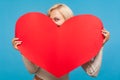 Playful blond girl peeping from big paper red heart in her hands, saint valentines day celebration, love and fondness