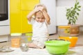 Playful child boy with face in flour surrounded kitchenware and foodstuffs