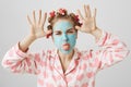 Playful and childish cute girl in facial mask and hair-curlers, wearing nightwear with heart print, making faces and Royalty Free Stock Photo