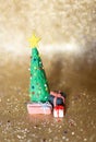 Playful clay christmas concept. Colorful handmade miniature Christmas tree and presents in gold background