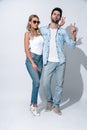 Playful couple. Full length of beautiful young couple in denim wear making peace sign while standing against grey background