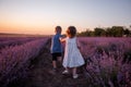 Playful cute boy girl are playing in rows of lavender purple field at sunset. Small couple. Allergy