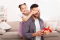 Playful daughter surprising her dad, closing his eyes and giving gift