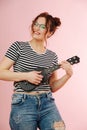 Playful eccentric woman with black ukulele over pink background