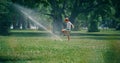 Playful elementary age boy kicking water sprinkler jet. Kid enjoy time in park Royalty Free Stock Photo