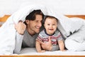 Playful father hiding under blanket with baby son