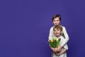 Playful friendly hug of two cheerful children, boy and girl, dressed in beige casual clothes, with tulips in their hands on purple