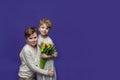 Playful friendly two cheerful children, boy and girl, dressed in beige casual clothes, with tulips in their hands on purple