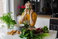 Playful and funny blonde woman holding sprout onion like mustache. Humorous cooking of mixed eco vegetable salad at home