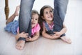 Playful girls holding father's legs on hardwood floor Royalty Free Stock Photo