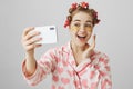 Playful good-looking girl at home making beauty procedures, wearing hair-curlers, nightwear and eye patch mask, smiling Royalty Free Stock Photo