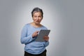 Playful grey haired mature woman with digital tablet working or checking on social media. Pretty woman in 50s in blue Royalty Free Stock Photo