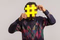 Playful happy african guy with dreadlocks in trendy sweatshirt hiding face behind hashtag symbol, popular blogger recommending to