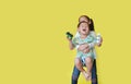 Playful of happy asian sister hugging and lift up her little brother standing on yellow background with copy space Royalty Free Stock Photo