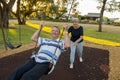 Happy senior American couple around 70 years old enjoying at swing park with wife pushing husband smiling and having fun together Royalty Free Stock Photo