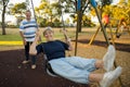 Happy senior American couple around 70 years old enjoying at swing park with wife pushing husband smiling and having fun together