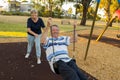 Happy senior American couple around 70 years old enjoying at swing park with wife pushing husband smiling and having fun together Royalty Free Stock Photo