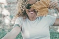 Playful happy woman portrait smiling and hidden half face with big autumn dry yellow maple leaf. Cheerful young adult female Royalty Free Stock Photo