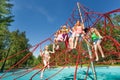 Playful kids sit on red ropes of playground