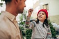 Playful little girl in red cap is sitting outdoor and pretend to drawing on her dad`s face. Father enjoying the time together wit Royalty Free Stock Photo