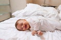 Playful lovely baby boy in white clothes, smiling and laughing lying on white bedsheets on the bed at home